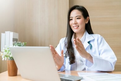 young attractive asian female doctor diagnosis talking and looking to camera in video conference ,positive doctor waving and having online consultation on digital tablet laptop