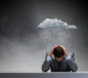 depressed young businessman sitting wet under rain