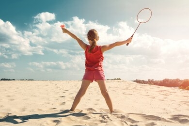 the concept of sport and active play in the summer. little girl playing beach badminton in the sunny day. the view from the back.