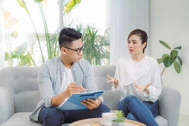 smiling young asian male psychiatrist talking to young woman at his office.