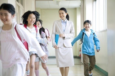 primary japanese boy and japanese girl who are playing with a female teacher walking the corridor