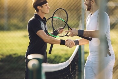 professional tennis players shaking hands at the net. two sportsmen shaking hands over the net after the match.
