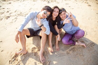 asian teenager is sitting by the beach with friends. a group of friends are sitting on the beach to play in the sea. travel with friends concept