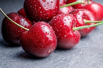 pile of dark red cherries with fine water splashes on each cherry on light grey background, close up shot, soft reflections with moody soft shadows