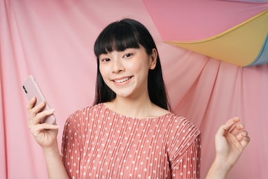 beautiful asian thai long dark hair woman in pink dress enjoy life using smartphone over pink summer background. fashion portrait.