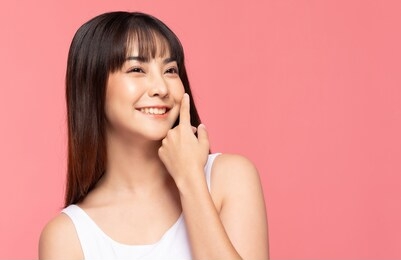 young beautiful asian woman smile touching soft cheek with clean and fresh skin happiness and cheerful with positive emotional,isolated on pink background,beauty cosmetics and spa treatment concept