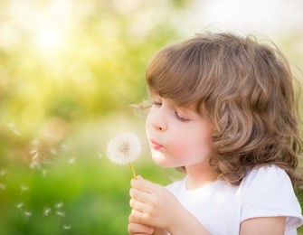 happy child blowing dandelion outdoors in spring park
