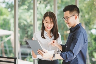 entrepreneur asian businessman and woman discussing new business project in tablet in modern meeting room. image focused on woman