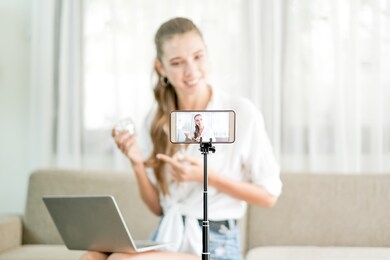 beautiful woman with white shirt show and live review the cosmetic product in front the camera from mobile phone with concept of shopping online and new normal lifestyle.
