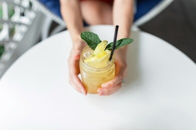 summer delicious lemonade in a vintage mug on a white table on the terrace. female hands hold yellow fresh cold lemonade drink with mint