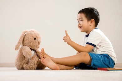 asian boy with teddy bear, vietnamese toddler pointing and talking to stuffed toy, cute kid sitting on floor communicating with his favorite toy friend
