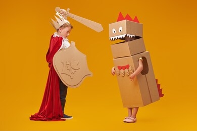 portrait of a cute boy in costume of knight with cardboard armour is fighting the cardboard dragon. childhood dreams. full length portrait on a yellow background.