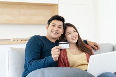 asian couple siting on sofa happy for payment purchase movie online by credit card with kitchen room background