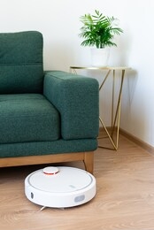 robotic vacuum cleaner cleaning laminate wooden floor in living room. smart cleaning technology. housework and technology concept. vertical