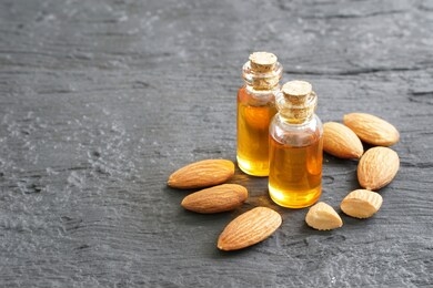 almonds oil in clear glass bottles and pile of roasted almonds on black wooden plank, blank space in the left side, copy space concept.