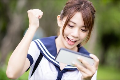 asian high school student girl use mobile to play game happily on campus