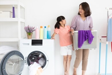 mother and child girl little helper are having fun and smiling while doing laundry at home