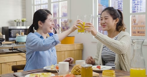 relax asian japanese female friends clink glasses in home kitchen during breakfast.