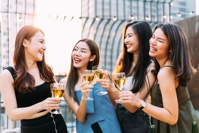 focus on glasses: group of happy asian girl friends celebrating party with champagne toasting drinks at outdoor restaurant together, enjoy chatting, laughing with smile. young people lifestyle 