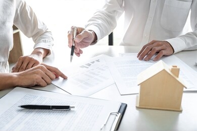 real estate broker agent presenting and consult to customer to decision making sign insurance form agreement, home model, concerning mortgage loan offer for and house insurance.