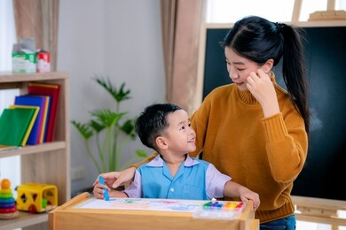 asian teacher in classroom on preschool teach her student to drawing on paper by color pencil on the table with backbord background, this image can use for back to school and education concept.