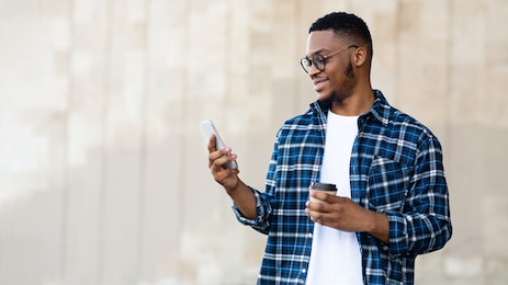 technology concept. young successful afro designer reading good news from friends on phone and enjoying morning coffee