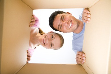 young smiling couple looking into cardboard box. they're looking at camera. low angle view.