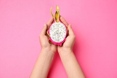 woman holding half of delicious ripe dragon fruit (pitahaya) on pink background
