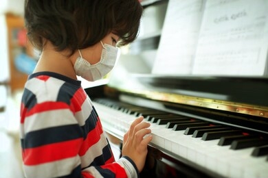 child wearing face mask playing piano at home.fingers on keys.boy having music lesson.young male musical homeschooling.string instrument.