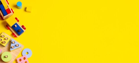 baby kids toys banner background. wooden train, educational stacking color recognition puzzle toy and colorful blocks on yellow background. top view