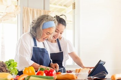 senior asian mother and middle aged daughter cooking together at kitchen