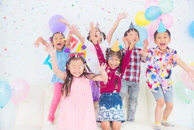 group of happy asian kids raise hands up and enjoy throwing colorful confetti with friends in birthday party.