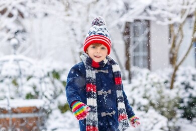 cute little funny child in colorful winter fashion clothes having fun and playing with snow, outdoors during snowfall. active outdoors leisure with children. kid boy and toddler catching snowflakes.
