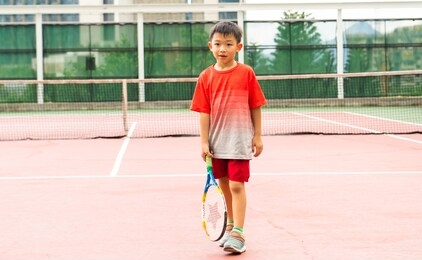 one lovely asian boy is playing the tennis in the outdoor court with fun. healthy kid with the exercise activity.