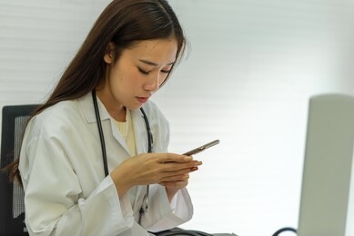young asian female doctor using mobile phone on the desk.