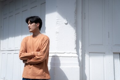 handsome asian guy wearing long sleeve t-shirt orange color standing in front of white door background with copy space