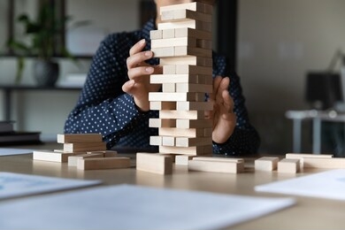 close up young indian woman constructing tower with wooden bricks alone in office, sitting at table. female employee manager developing strategic thinking skills or challenging at workplace.