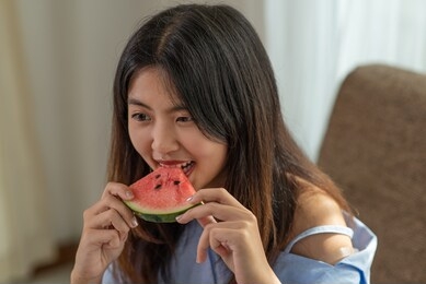 portrait happy young asian woman is enjoy eating slice of watermelon
