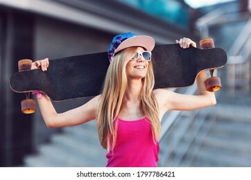 young attractive girl with skateboard standing outdoors in skate park.