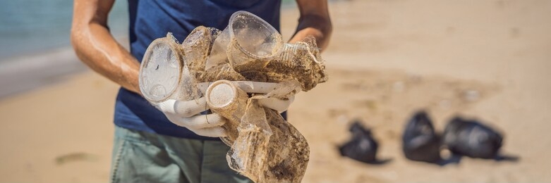 man in gloves pick up plastic bags that pollute sea. problem of spilled rubbish trash garbage on the beach sand caused by man-made pollution and environmental, campaign to clean volunteer in concept