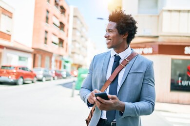 young african american businessman wearing suit smiling happy. standing with smile on face using smartphone at town street.