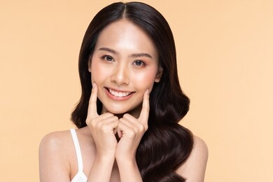 beautiful asian young woman touching soft cheek smile with clean fresh skin happiness and cheerful with positive emotional,isolated on beige background,beauty cosmetics and facial treatment concept