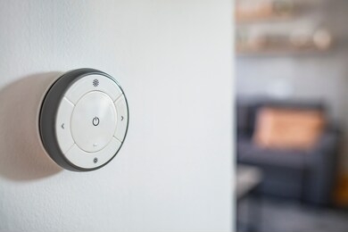 round smart thermostat with touch screen installed on the wall indoors. smart home heating regulation concept. view with copy space