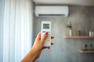 air conditioner inside the room with woman operating remote controller. / air conditioner with remote controller. close up view of hand operating air conditioner remote control. 