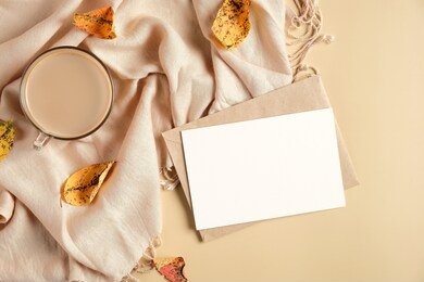 autumn flat lay composition with blank paper card, letter envelope, coffee cup, scarf, fallen leaves on beige background. autumn hygge style desk table, top view.