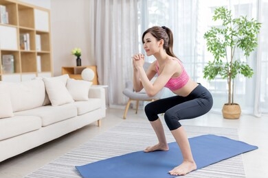 asian young woman is doing squats exercise at home