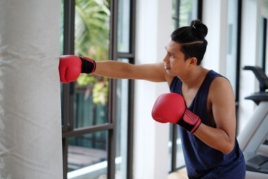 an asian sport man wearing red boxing gloves punching heavy bag at training fitness gym.