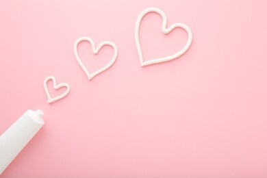 heart shapes created from cream. white tube on light pink table background. pastel color. care about face, hands, legs and body skin. closeup. empty place for text or logo.