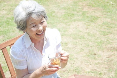 a senior japanese woman laughs as she takes tea in the garden