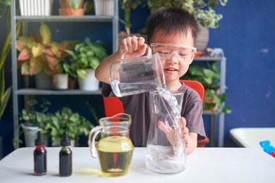 happy little asian school kid studying science, making diy lava lamp science experiment with oil, water and food coloring, kid-friendly fun and easy science experiments at home concept